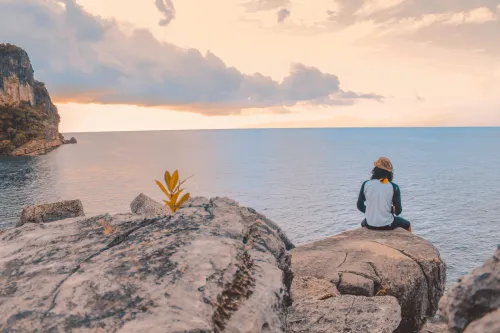 Eine Person steht auf einem Felsen, schaut auf den Horizont und überwindet symbolisch Herausforderungen